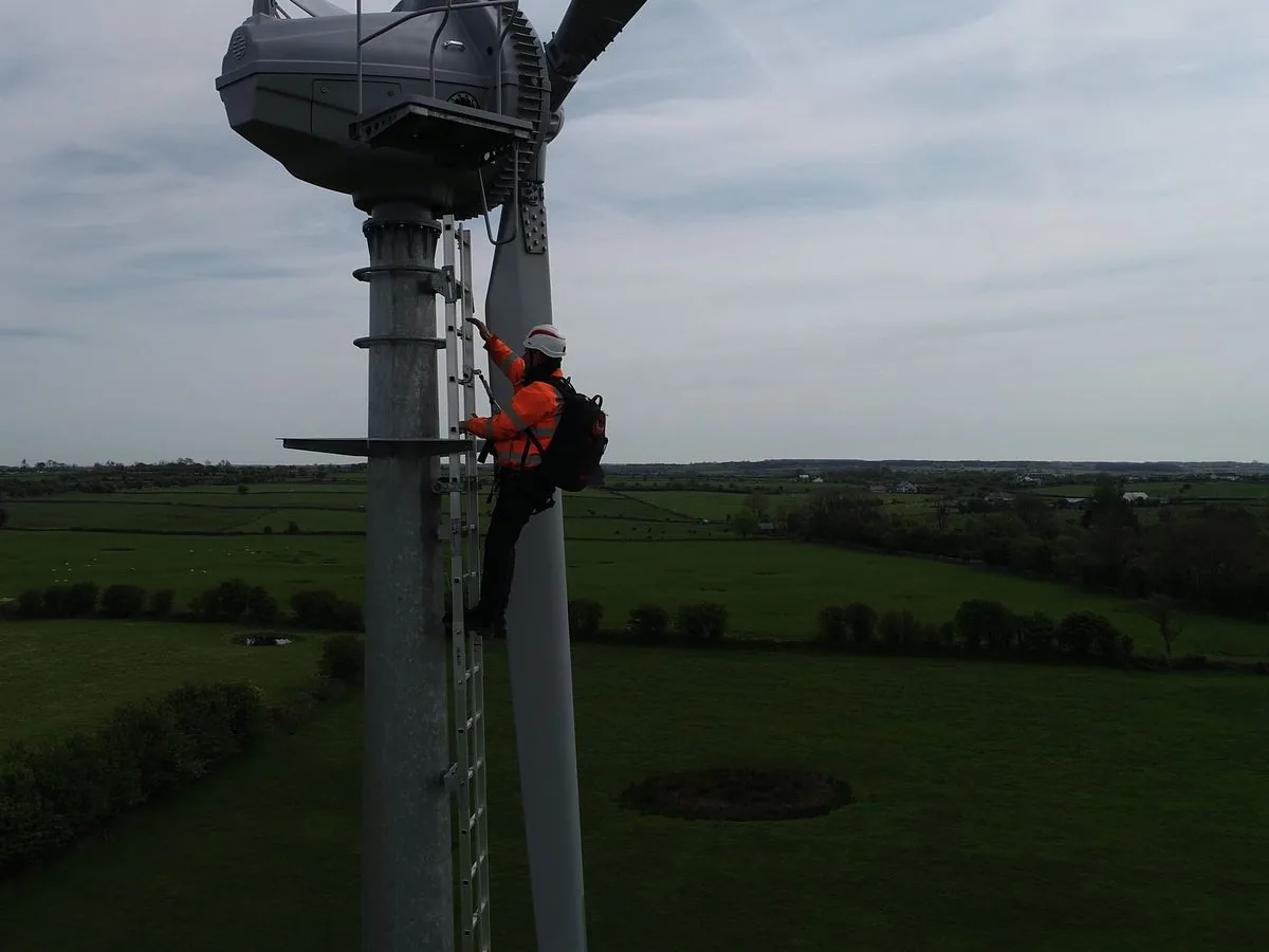 A technician climbing the tower ladder up to the working platform below the nacelle