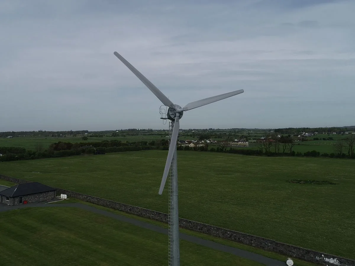 A Kodair turbine in open farmland beside farm buildings
