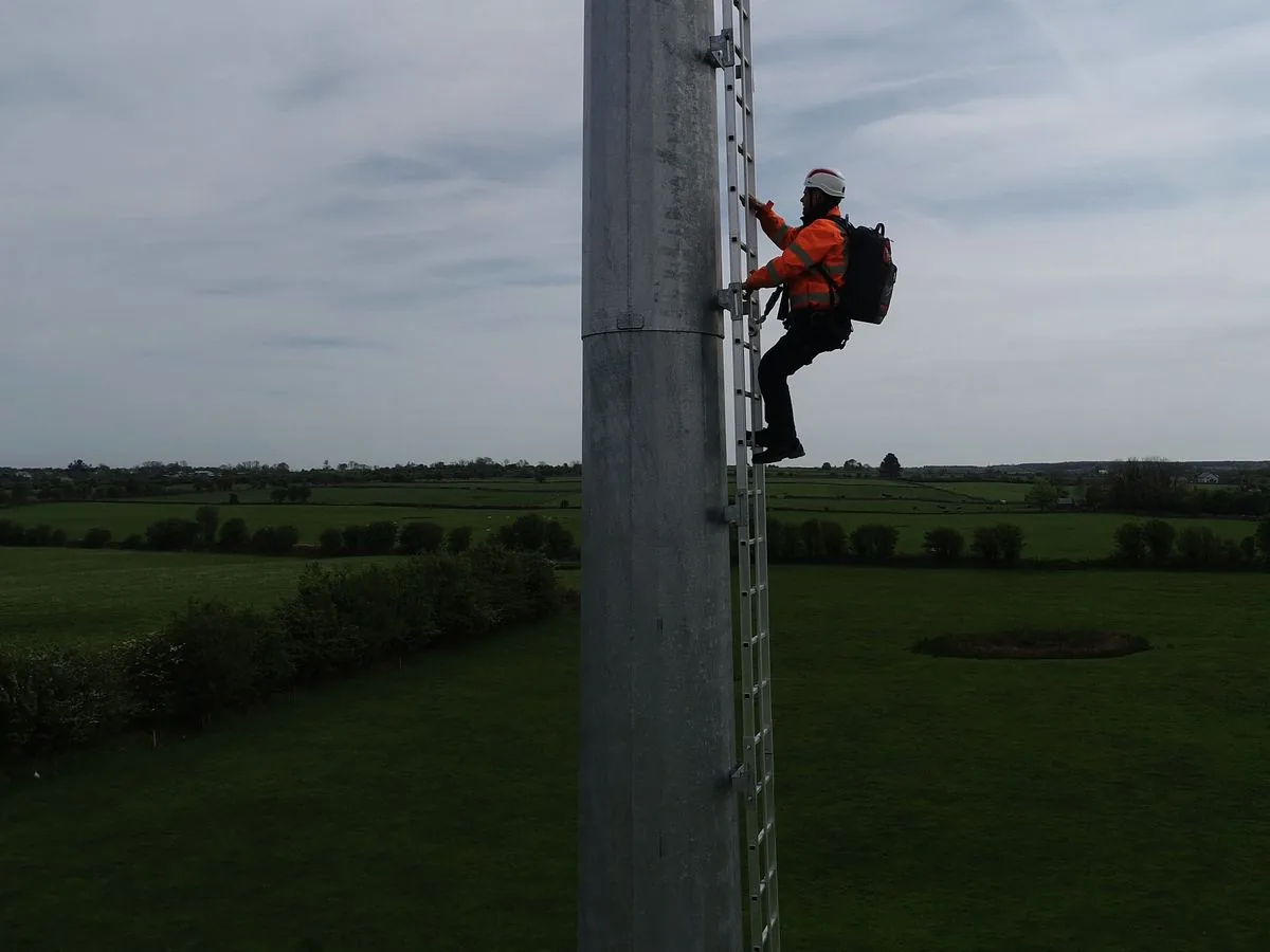 A technician in a safety harness climbing the tower ladder